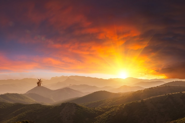 Majestätischer Sonnenuntergang über Bergen und einsamer Windmühle, schöne Landschaft