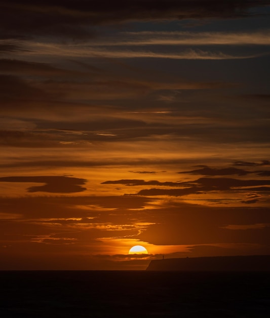 Majestica puesta de sol con siluetas de acantilados y faro en el mar