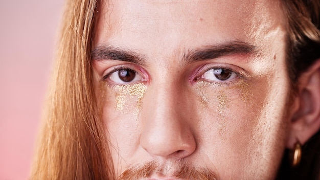 Foto make-up-augen und porträt eines gen z-mannes mit ernstem ausdruck im gesicht mit rosafarbenem hintergrund goldene glitzertränen und kunstzoom auf augenkosmetik auf nicht binären transgender- oder geschlechtsneutralen lgbt-modellen