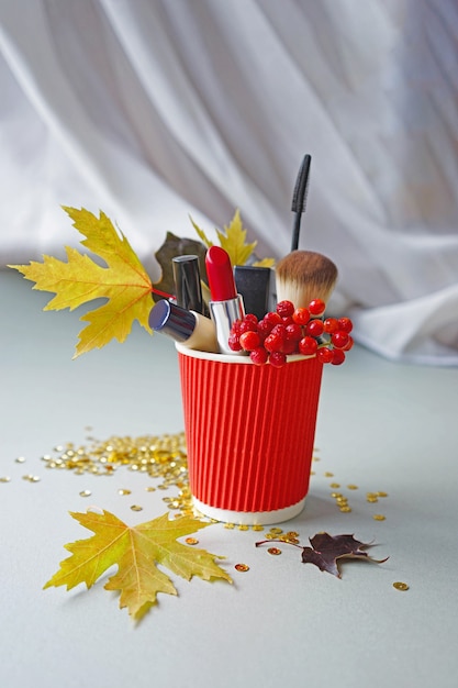 Make-up-Kosmetik in einer roten Tasse mit gelbem Herbstlaub