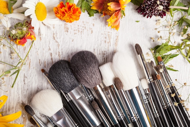 Make-up-Pinsel auf Holzuntergrund neben Wildblumen. Professionelle Kosmetik