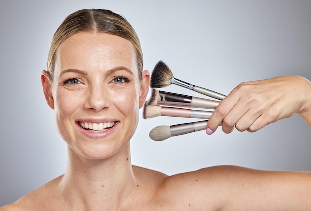 Make-up-Pinsel für Frauen und Porträtlächeln für kosmetische Schönheits- oder Gesichtsbehandlungen vor einem Studiohintergrund Glückliches Gesicht des weiblichen Modells, das in der Hautpflege lächelt und Make-up-Tools für die Selbstpflege hält