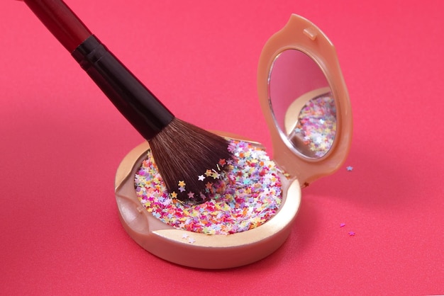 Make-up-Puder und Kosmetikpinsel mit bunten Glitzersternen auf rotem Grund