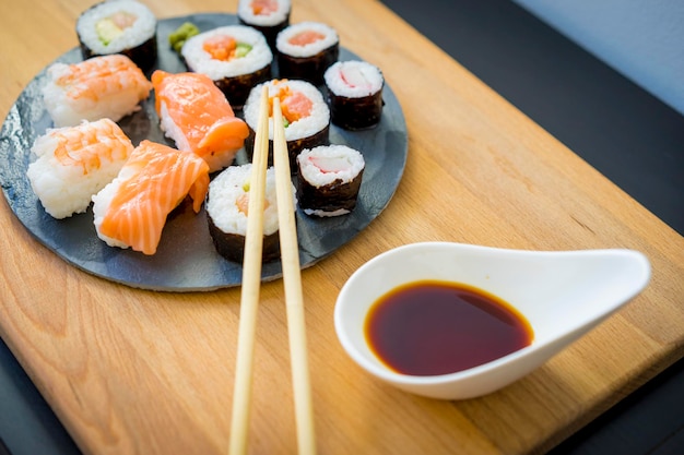 Maki em uma mesa de madeira na placa de ardósia preta com molho de soja e pauzinhos