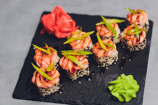 Maki Sushi Rolls mit Lachs auf schwarzem Stein auf dunklem Hintergrund. Mit Ingwer und Wasabi. Sushi-Menü. Japanisches Essen. Nahaufnahme des köstlichen japanischen Essens mit Sushi-Rolle. Horizontales Foto.