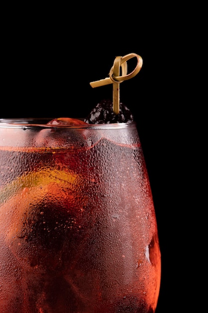 Makro-Nahaufnahme auf Cocktailglas mit Rosato-Roséwein und Beeren als Beilage und Eis isoliert auf schwarzem Hintergrundtisch von oben gesehen