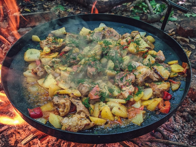 Makro-Nahaufnahme von Bratkartoffeln mit Fleisch und Gemüse in einer Pfanne über einem Feuer