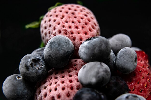 Makroansicht von gefrorenen Beeren: Erdbeere, Blaubeere mit Eiswürfeln