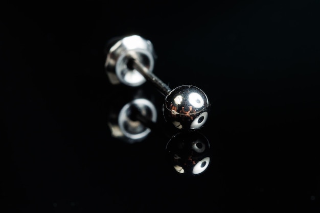 Makrofoto des silbernen Ohrrings mit einem Edelstein auf einem schwarzen lokalisierten Hintergrund