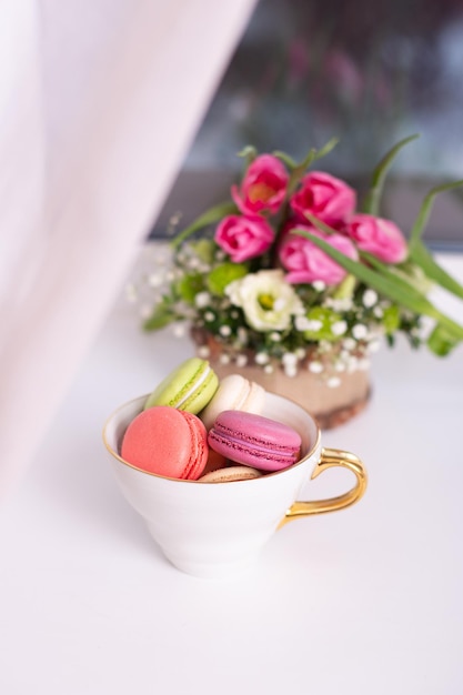 Makronen des süßen Nachtischs im goldenen Becher und in den rosa Tulpen auf Fensterhintergrund