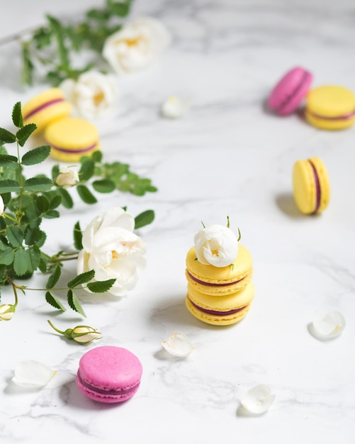 Makronen und Blumen Französisches Essen Gelbe und rosa Makronen auf einem Marmortisch Französisches Dessert