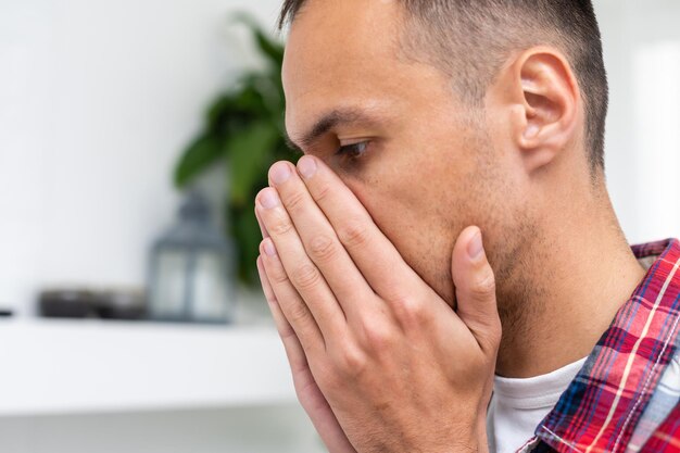 Mal aliento. Concepto de halitosis. Hombre joven que controla su respiración con la mano.