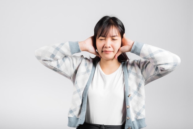 El mal humor de la mujer le duele los oídos cerrados con las palmas de las manos y los ojos cerrados, la hermosa joven asiática cubre los oídos por ruido fuerte, toma de estudio aislada en fondo blanco con espacio para copiar