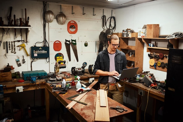 Mal sehen, was das Internet sagt Schnappschuss eines konzentrierten jungen männlichen Tischlers, der an seinem Laptop arbeitet, während er nachts in seiner Werkstatt steht