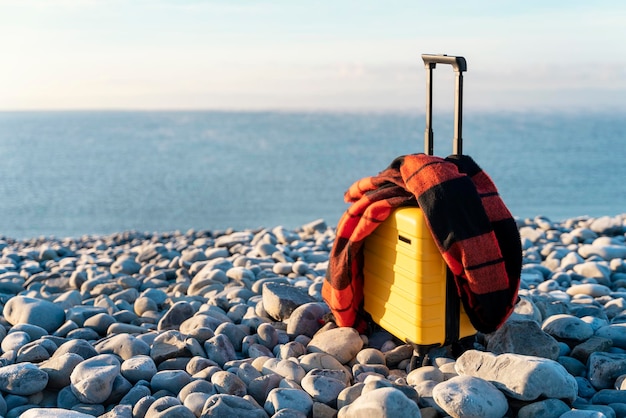 Mala amarela com um lenço laranja à beira-mar contra o mar Conceito de viagem