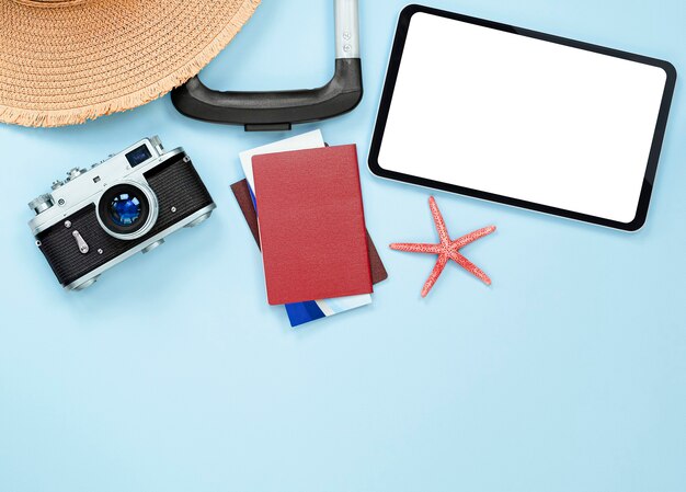 Mala, chapéu de sol, tablet, câmera, estrela do mar, passaporte e ingressos em um fundo azul claro