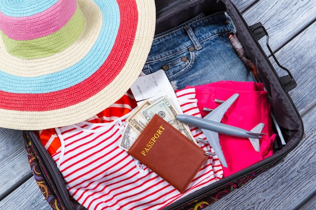 Mala com roupas e passaporte. Avião de brinquedo e chapéu de praia. Bagagem na prateleira de madeira. Passagem de avião para viagem de verão.