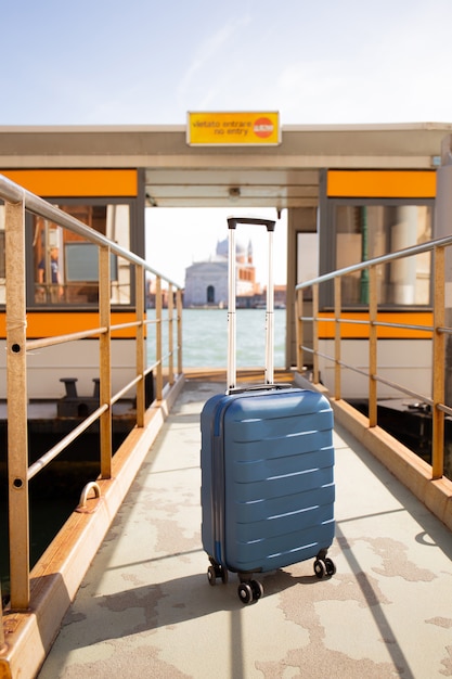 mala de viagem perto de ônibus fluvial em dia de sol em Veneza, Itália.