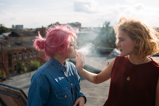 Mala influencia. Chica fumando un cigarrillo de la mano de su amiga. Estilo de vida adolescente de la calle. Peligros de las malas asociaciones