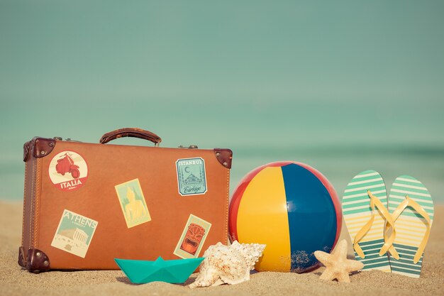 Mala vintage e chinelos na praia contra o azul do mar e do céu