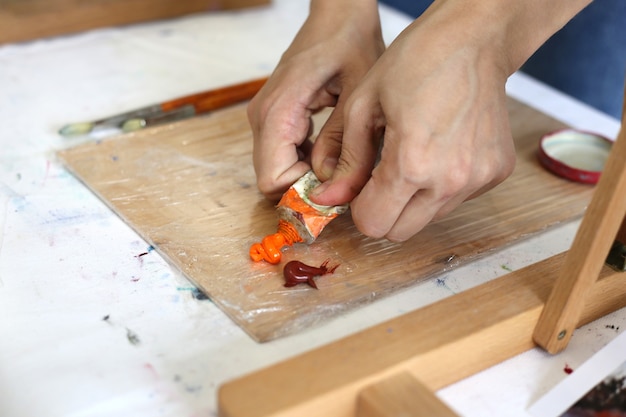 Malerhände drücken orangefarbene Ölfarbe auf eine Holzpalette