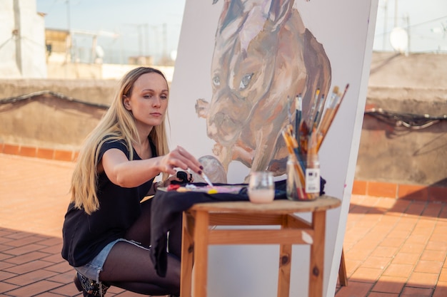 Malerin der jungen Frau, die zu Hause Dach zeichnet. Bild der Bulldogge auf großer Leinwand. Kunst im Freien