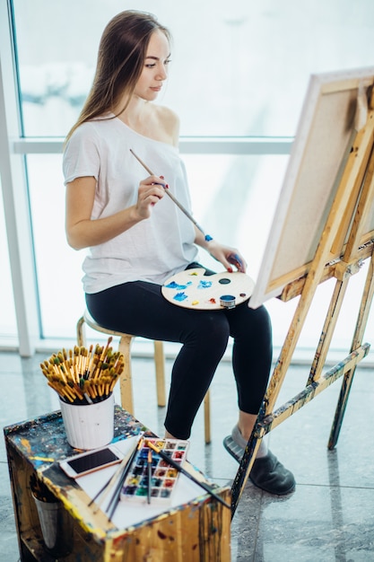 Malerin, europäisches Mädchen, das Seelandschaft auf Leinwand in ihrer Werkstatt zeichnet. Konzept des Kunstunterrichts