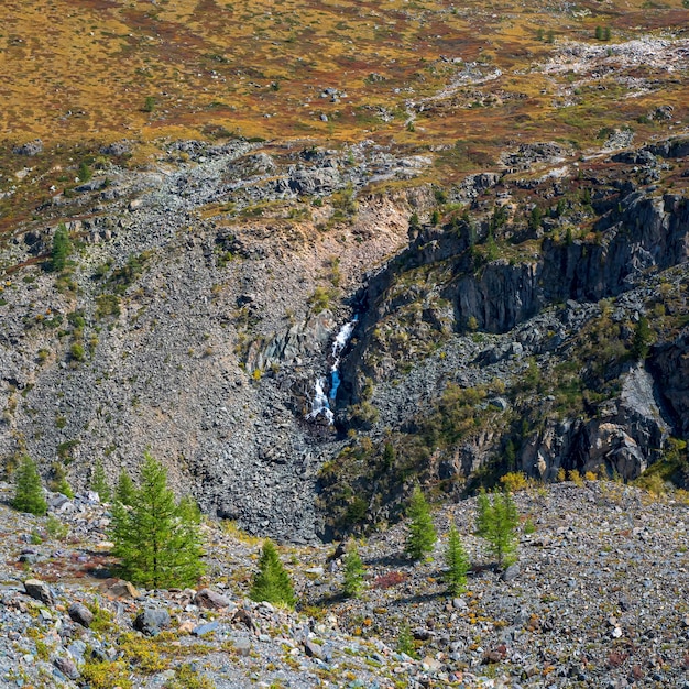 Malerische Alpenlandschaft mit Bäumen im Tal und großer Bergkette mit Wasserfall im sonnigen Licht. Bunte Naturlandschaft mit schönen Bergen. Blick auf den Platz.