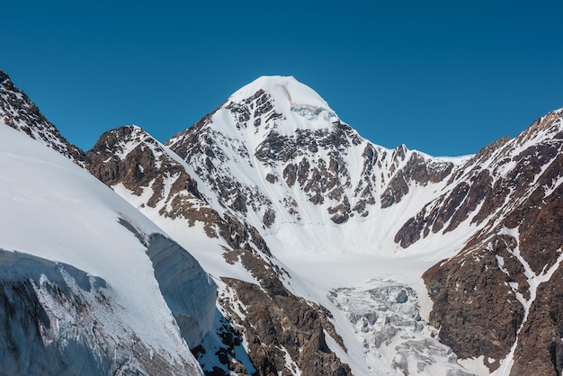 Malerische Alpenlandschaft mit schneebedeckter Bergspitze und steiler Gletscherzunge mit Eisfall im Sonnenlicht Ehrfürchtige Berglandschaft mit spitzem Gipfel und Gletscher auf Felsen unter blauem Himmel an sonnigen Tagen