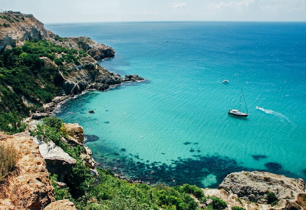 Malerische Ansicht von blauem sauberem Meer, von Felsen, von sich hin- und herbewegendem Boot und von grünen Bäumen.