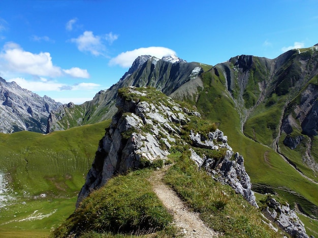 Malerische Aussicht auf einen Wanderweg an Berghängen im Sommer mit felsigen Gipfeln und blauem Himmel. Touristische Landschaften