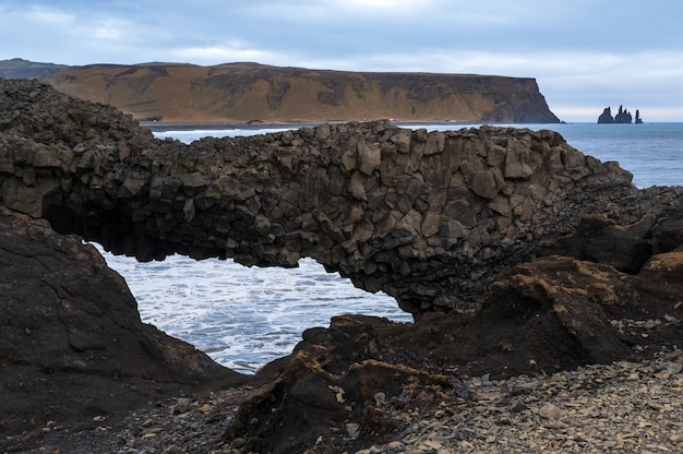 Malerische Herbstabendansicht zum Reynisfjara-Ozean, schwarzem Vulkansandstrand und Felsformationen von Dyrholaey Cape Vik South Island Mount Reynisfjall im Hintergrund