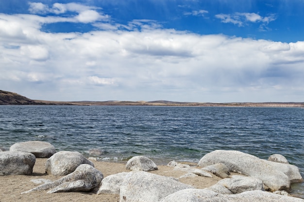 Malerische Landschaft in nationalem Naturpark Burabay, Kasachstan-Natur. Ufer des Lake Big Chebachie, große Steine, Sand und Wasser. Mai 2019.