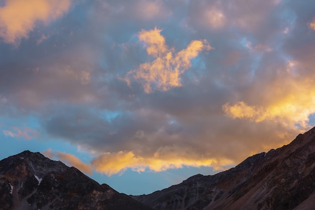 Malerische Landschaft mit dunkler Bergkette Silhouette unter blauem Abendhimmel mit leuchtend orangefarbenen Sonnenuntergangswolken Sonnendurchflutete orange Cirruswolken im Sonnenunterganghimmel über Bergsilhouetten bei wechselhaftem Wetter