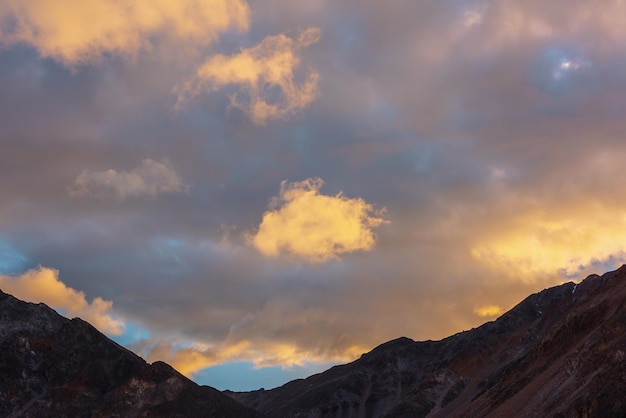 Malerische Landschaft mit dunkler Bergkette Silhouette unter blauem Abendhimmel mit leuchtend orangefarbenen Sonnenuntergangswolken Sonnendurchflutete orange Cirruswolken im Sonnenunterganghimmel über Bergsilhouetten bei wechselhaftem Wetter