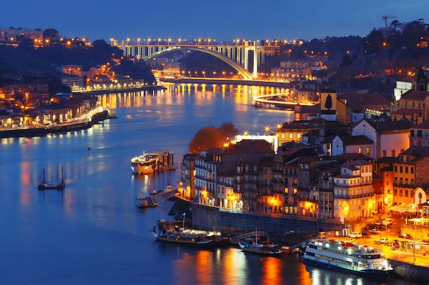 Malerische Luftaufnahme der Altstadt von Porto, Ribeira und Brücke mit Spiegelreflexionen im Fluss Douro während der blauen Abendstunde, Portugal