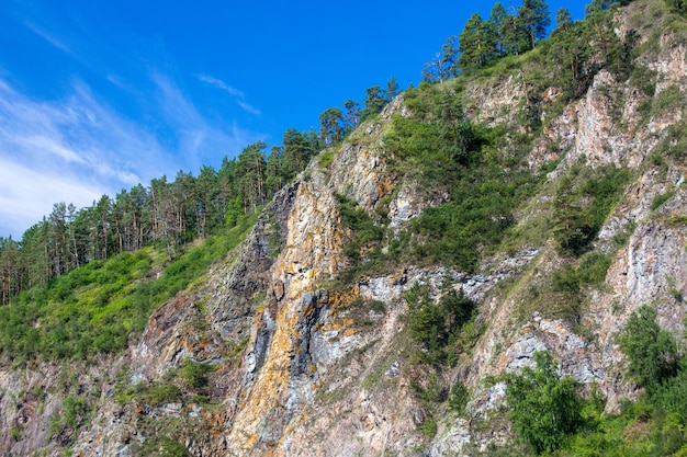 Malerische, mit Nadelwäldern bedeckte Felsen vor einem blauen Himmel mit weißen Wolken