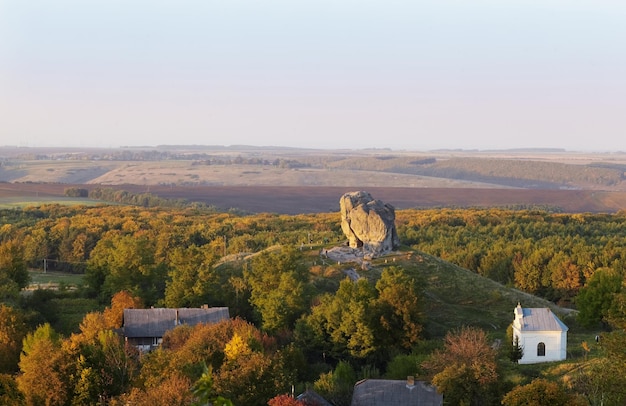 Malerischer Blick auf den Inselberg Pidkamin auf dem angrenzenden Hügel und dem nahe gelegenen Dorf in der Region Brody in Galychyna, Ukraine