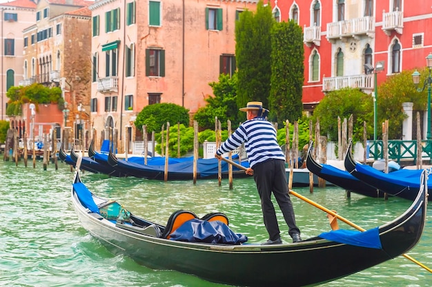 Malerischer Blick auf Gondeln am Canal Grande in Hut mit blauem Band und typisch gestreiftem Unterhemd Venedig Italien Selektiver Fokus auf Gondoliere