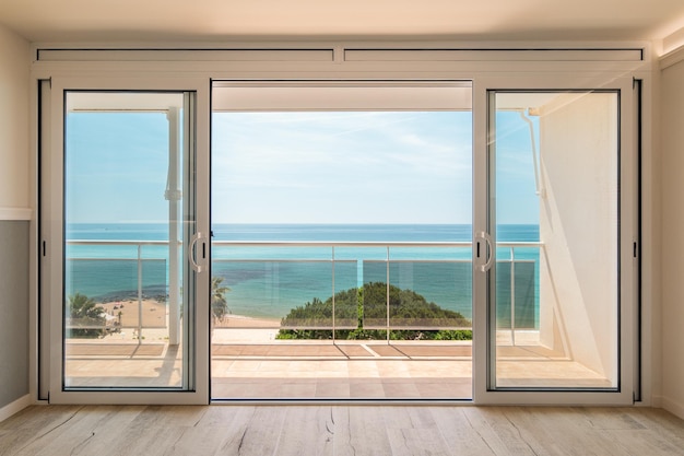 Malerischer Blick von einem Gästehaus durch Panoramafenster mit Terrasse auf das Meer bei sonniger Wärme