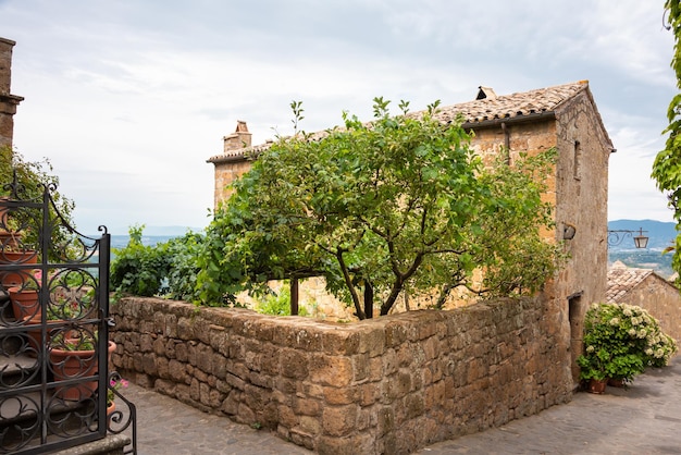 Malerisches Haus und Garten mit Bäumen in einer mittelalterlichen Stadt in der Toskana, Italien. Alte Steinmauer