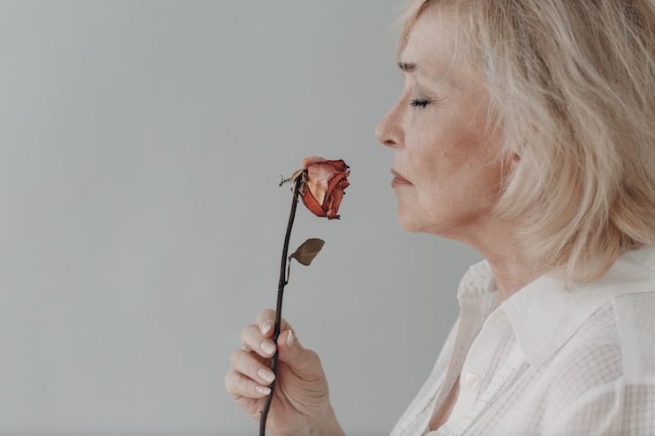 Malestar anciana vestida de blanco mantenga marchito una vieja flor rosa seca