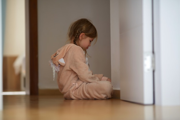 Malestar niña sentada en el piso cerca de la puerta