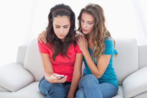 Malestas amigas leyendo mensajes de texto en casa
