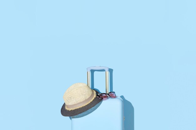 Maleta con gafas de sol y sombrero sobre fondo azul pastel Concepto de viaje Estilo minimalista