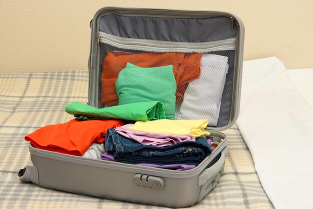 Foto maleta gris abierta con ropa en la cama