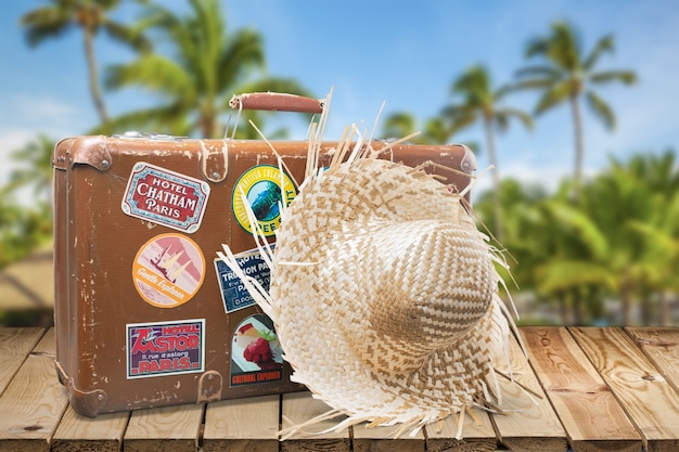 Foto maleta retro con sombrero de viaje sobre fondo tropical