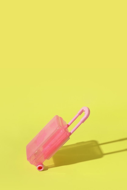 Maleta rosa de juguete sobre fondo amarillo con una sombra dura Espacio de copia Concepto de viaje o migración