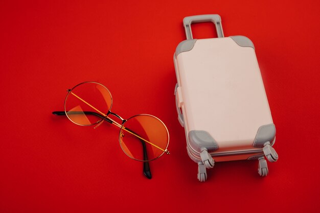 Maleta rosa con ruedas y gafas de sol amarillas. concepto de viajes y vacaciones