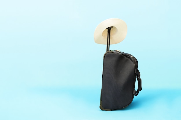 Foto maleta y sombrero sobre un fondo azul.